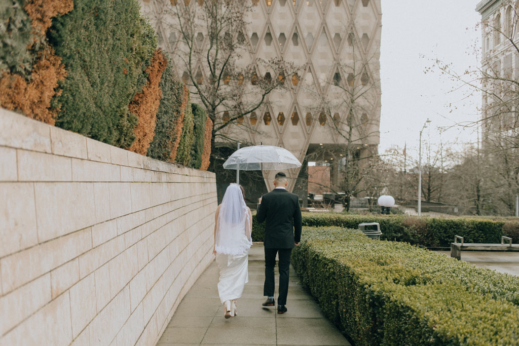 bride and groom holding an umbrella while walking through downtown seattle for an elopement