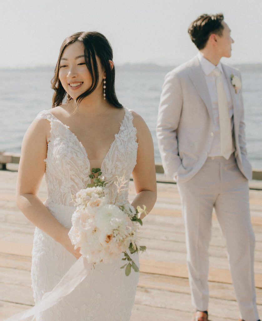 bride smiling while holding bouquet while groom is in the background