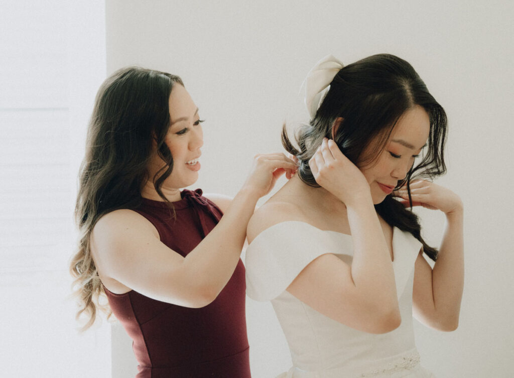 friend helping bride put on her necklace while getting ready at seattle airbnb