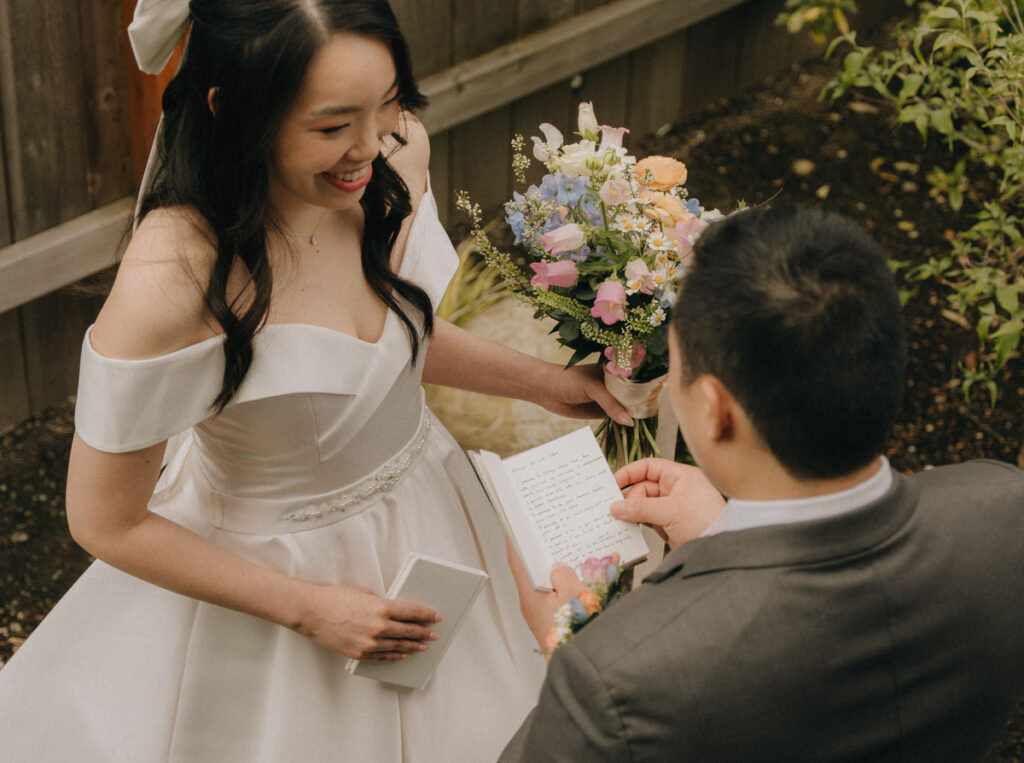 groom reading private vows to his bride who is smiling and holding flowers