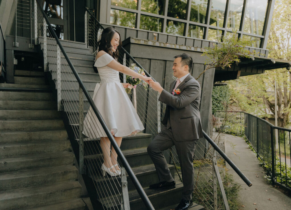 groom holding bride's hands at stairs in front of canlis in seattle